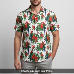 Man wearing a bold red Hawaiian shirt featuring parrots, hibiscus flowers, and big green leaves.
