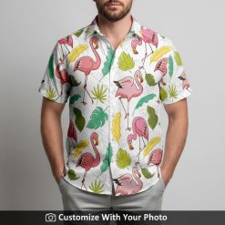 Man in white Hawaiian shirt featuring pink flamingos, vibrant leaves, and yellow accents