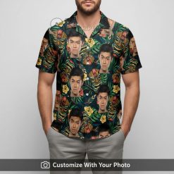 Hawaiian shirt with tiki mask face print, tropical flowers, green foliage worn by man by the shore
