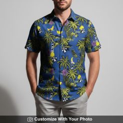 Man modeling blue Hawaiian shirt featuring palm tree, pineapple, and hibiscus motifs