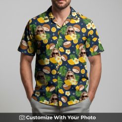 Man in navy and yellow Hawaiian shirt with face print, oranges, coconut, green leaves