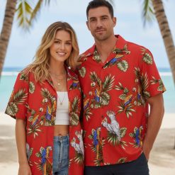 Male model in casual pose wearing parrot Hawaiian shirt in beach setting with palm trees visible