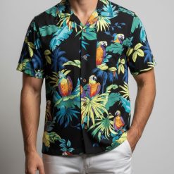 Model showcasing tropical parrot Aloha shirt in outdoor beach setting with vibrant bird pattern visible