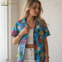 Blue aloha shirt featuring spotted pineapples in bright colors with tropical leaf accents on striped background