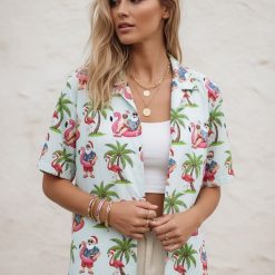 Xmas Hawaiian shirts with pattern of Santa Claus on flamingo pool floats holding drinks surrounded by palm trees and flamingo graphics
