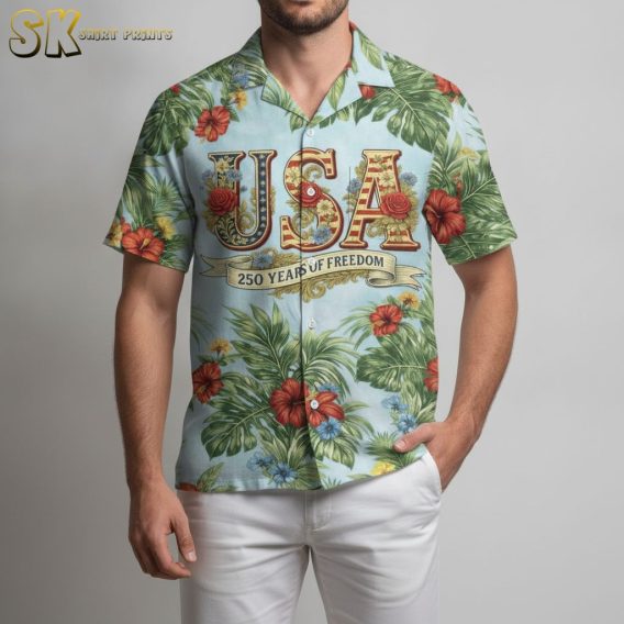 America 250th anniversary Hawaiian shirt with red yellow and blue tropical flowers, large green leaf print, USA lettering in red and gold, and a 250 Years of Freedom banner on a light blue background