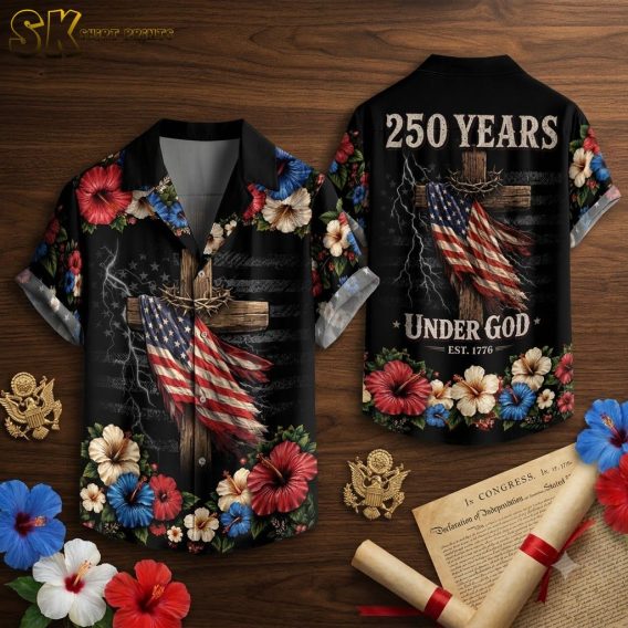 Flat lay of 250th anniversary Hawaiian shirt showing full print detail, black fabric with wooden cross wrapped in American flag, red white and blue hibiscus flowers, lightning accents, and back text elements