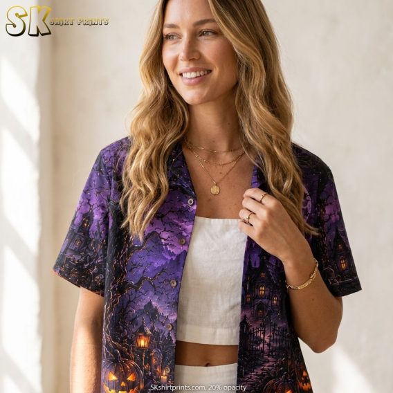 Female model wearing a light colorway Hawaiian shirt with Halloween costume print including a spooky castle, glowing jack-o'-lanterns, full moon, bats, and barren trees in purple and orange