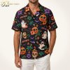 Halloween Hawaiian shirt with Summerween pattern including sunglasses-wearing ghosts, jack-o'-lanterns, hibiscus flowers, palm trees, and bats, shown on a male model against a warm white studio background