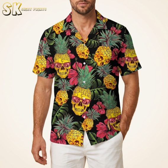 Men's black Hawaiian shirt with skull-faced pineapple and tropical leaf print photographed on male model against warm white studio background