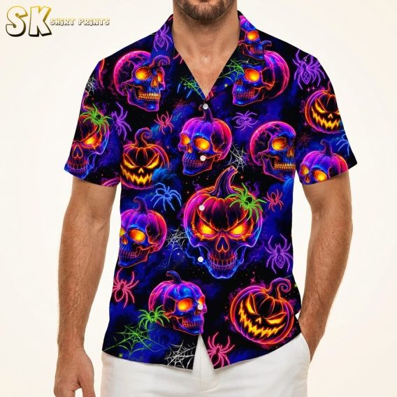 Man wearing a Halloween Hawaiian shirt with neon glowing skulls, jack-o'-lanterns, and spider webs on a dark background, photographed in studio against warm white background