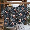 Christmas Hawaiian shirt displayed on hanger showing front and back, dark blue with repeated Santa hat faces, Christmas trees, snowflakes, and gold ornaments