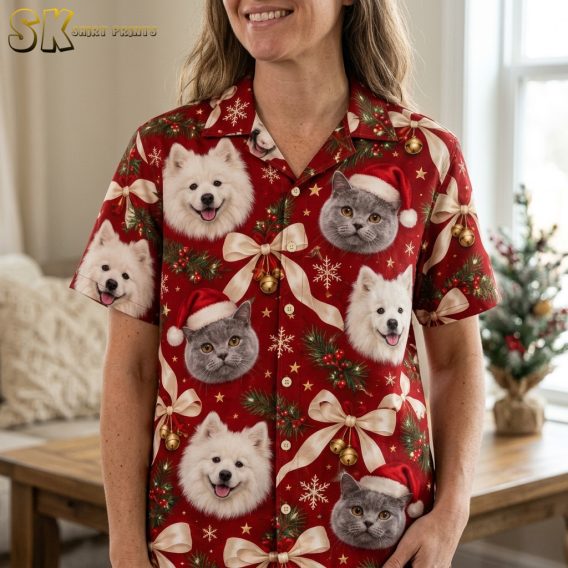 Close-up of a woman wearing a Christmas Hawaiian shirt womens style showing red background with dog and cat Santa hat portraits, gold bells, and pine branch details