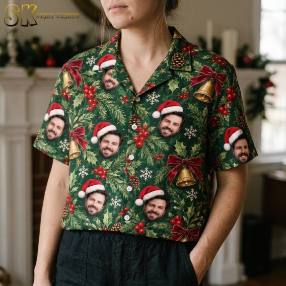 Close-up of a woman wearing a dark green family Christmas Hawaiian shirt showing Santa hat faces, holly leaves, berries, bells, and snowflakes in detail