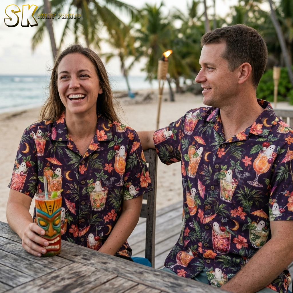 A couple wearing dark purple halloween hawaiian shirts printed with ghost-filled tropical cocktails, hibiscus flowers, palm leaves, and bats in a watercolor style.