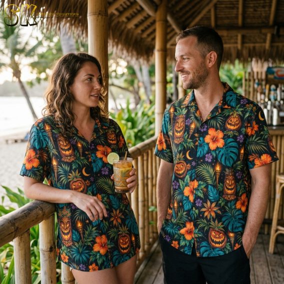 Couple wearing matching black halloween hawaiian shirts featuring tiki jack-o'-lantern faces, glowing torches, hibiscus flowers, and tropical foliage.