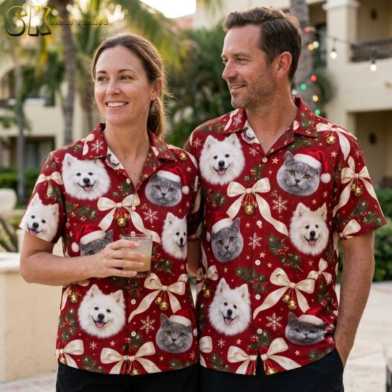 Couple wearing matching Hawaiian Christmas shirts with red dog and cat Santa hat print, gold bells, pine branches, and snowflake motifs