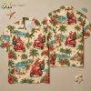 Flat lay of a hawaiian shirt with santa claus print showing front and back panels with Santa on a scooter, palm trees, hibiscus, Christmas trees, and beach huts on cream and red fabric