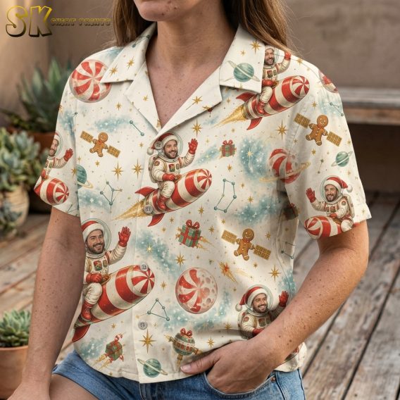 Closeup of a woman wearing a Hawaiian style Christmas shirt showing detailed astronaut Santa, candy cane rocket, gingerbread men, planets, and stars print in red, green, and cream