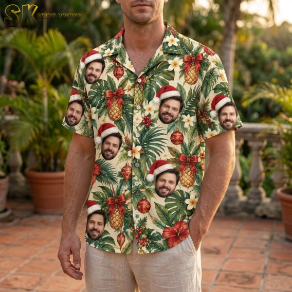 Man wearing a mens Christmas Hawaiian shirt with tropical Santa hat face print, hibiscus, pineapples, and red ornaments on beige fabric