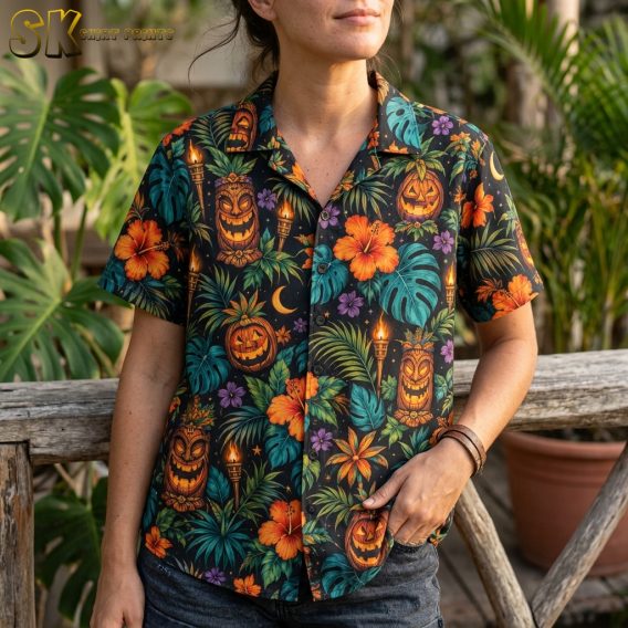 Close-up of a woman wearing a black spooky hawaiian shirt, showing detailed tiki jack-o'-lantern carvings, orange hibiscus, purple blossoms, and torch flame motifs.