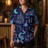 Female model in a closeup wearing a spooky Hawaiian shirt with neon green, orange, and purple haunted house, bat, and black cat print on navy blue fabric