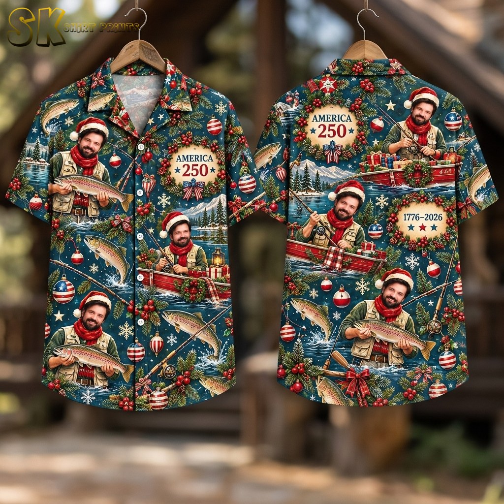 Flat-lay view of the shirt laid front and back on a flat surface, showing the full spread of the deep blue all-over print with the fishing Santa character in multiple poses, evergreen branches, snowflakes, American flag baubles, and the 'AMERICA 250' wreath graphic.