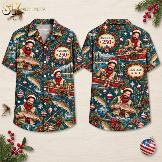 Front and back hanger view of a deep blue short-sleeve button-up shirt covered in an all-over print featuring a Santa-hat-wearing fisherman in a red boat, evergreen branches with red berries, American flag ornaments, snowflakes, and the text 'AMERICA 250' and '1776 – 2026' inside a Christmas wreath.