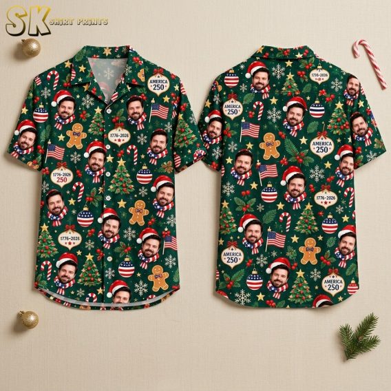 Front and back hanger view of a dark green short-sleeve button-up shirt covered in an all-over pattern of a bearded man's face in a Santa hat, decorated Christmas trees, gingerbread men, American flags, and ornaments reading AMERICA 250 with years spanning 1776 to 2026.
