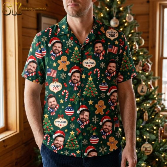 A man wearing the dark green short-sleeve button-up shirt featuring repeating photographic faces of a bearded man in a Santa hat, American flag scarves, and holiday ornaments labeled AMERICA 250.