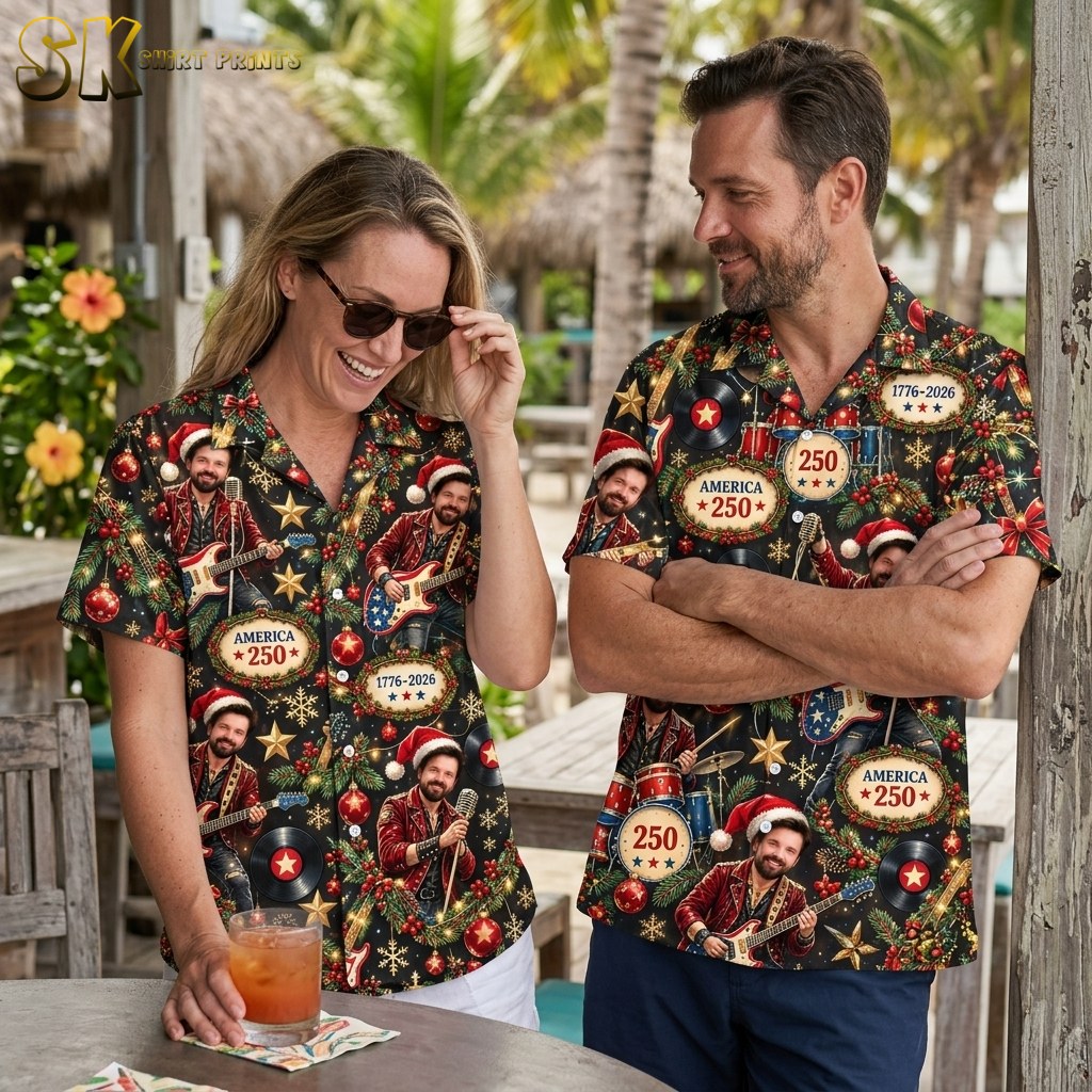 A couple shown together, with one person wearing the black camp collar shirt printed with a musician in a Santa hat, Christmas ornaments, gold stars, and America 250 anniversary references.