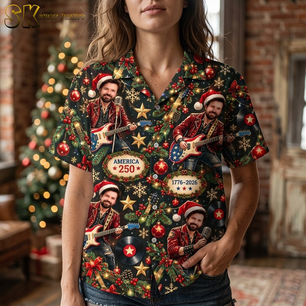 A close-up view of a woman wearing the black shirt, bringing the detailed pattern into focus and showing motifs such as holly leaves, red ornaments, vinyl records, and the America 250 text up close.
