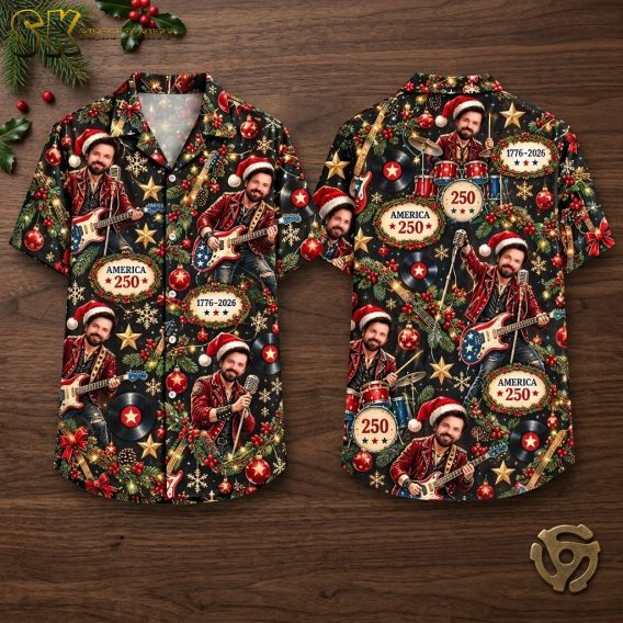 Front and back hanger view of a black short-sleeve button-up camp collar shirt covered in a dense all-over pattern of a man in a Santa hat playing guitar or drums, with Christmas ornaments, holly, snowflakes, and repeated text reading AMERICA 250 and 1776-2026.