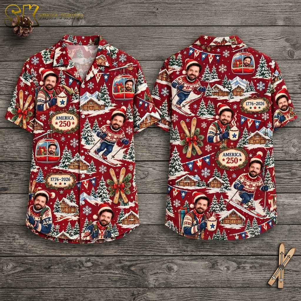 Both sides of a deep-red short-sleeve button-up shirt displayed on a wooden hanger, showing repeated printed faces of a smiling man in a Santa hat skiing, gondola cabins, crossed skis with a red ribbon, and emblem plaques reading AMERICA 250 and 1776-2026.