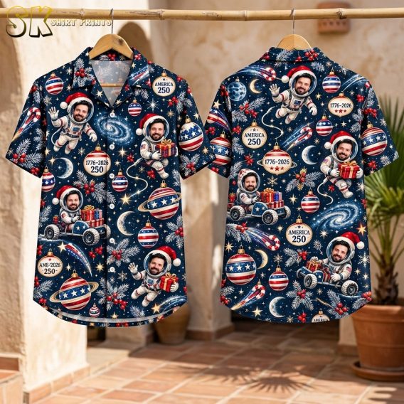 Front and back flat-lay view of the navy short-sleeve button-up shirt, showing the densely packed all-over pattern of Santa-hat-wearing astronauts, ringed planets, comets, candy canes, and patriotic ornaments laid out flat.
