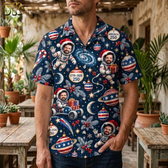 A man wearing the dark navy short-sleeve button-up shirt featuring astronauts in Santa hats, patriotic ornaments, and America 250 badges spread across an all-over pattern.