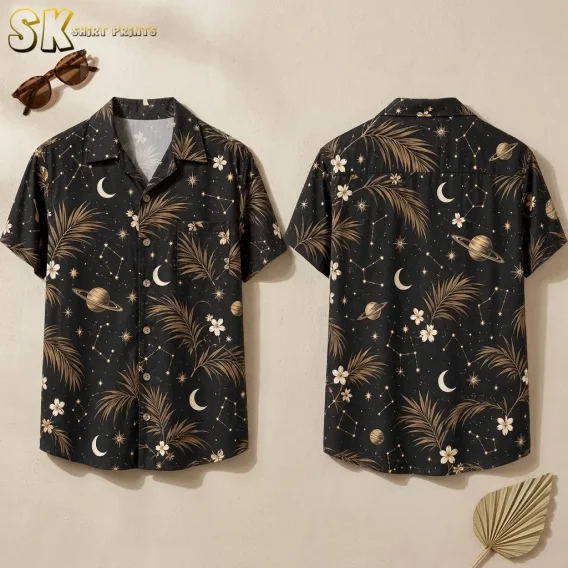 Front and back of a black short-sleeve button-up shirt with tan palm leaves and cream celestial motifs, arranged beside sunglasses.