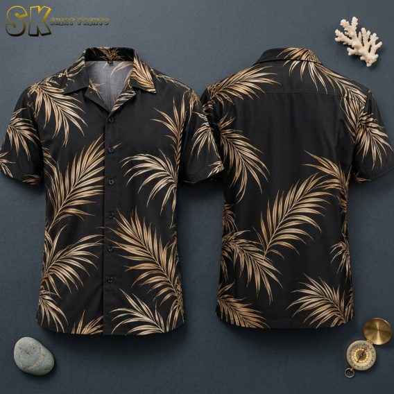 Front and back views of a black short-sleeve button-up shirt printed with large beige and tan palm fronds, displayed flat against a dark gray surface alongside a coral piece and compass.