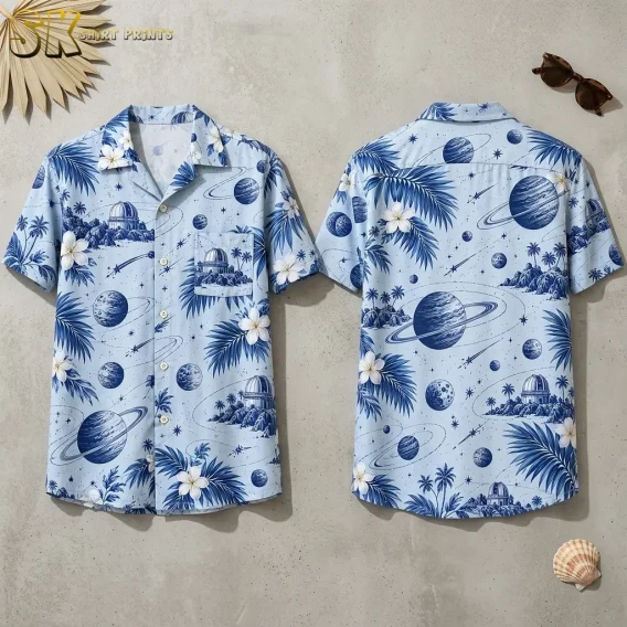 Front and back of a light blue short-sleeve shirt lie side by side, showing ringed planets, palm fronds, and white flowers.