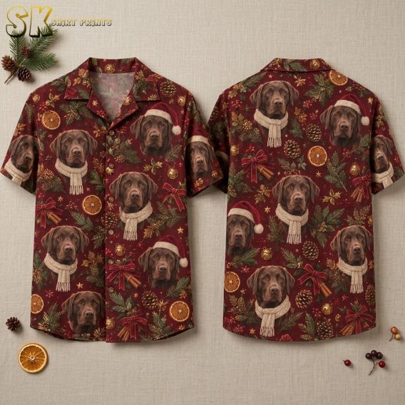 Front and back of a burgundy hawaiian style christmas shirt laid flat on a neutral surface, showing realistic chocolate Labrador faces wearing Santa hats and knitted scarves surrounded by pinecones, dried orange slices, and red bows.