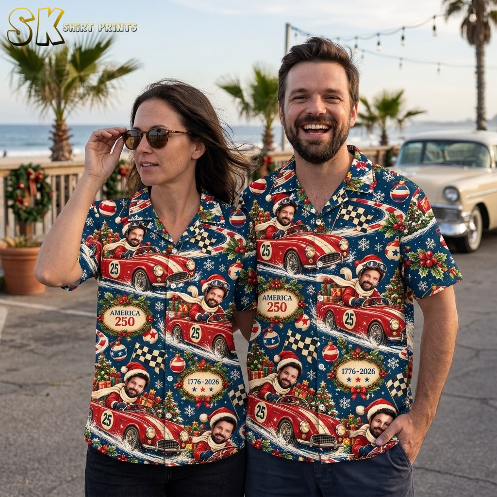 A woman and a man stand side by side near a coastal boardwalk, both wearing the same dark blue vintage race car Christmas shirt, with palm trees and a classic car visible in the background.