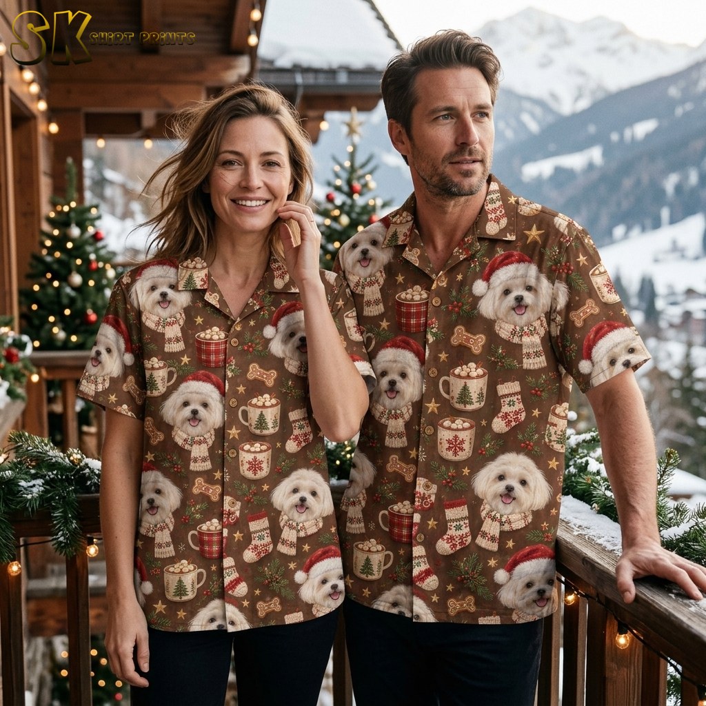 A man and woman stand together on a snow-dusted balcony with mountain peaks behind them, both wearing the same brown Maltese dog Christmas shirt, showing how the pattern scales across different fits.