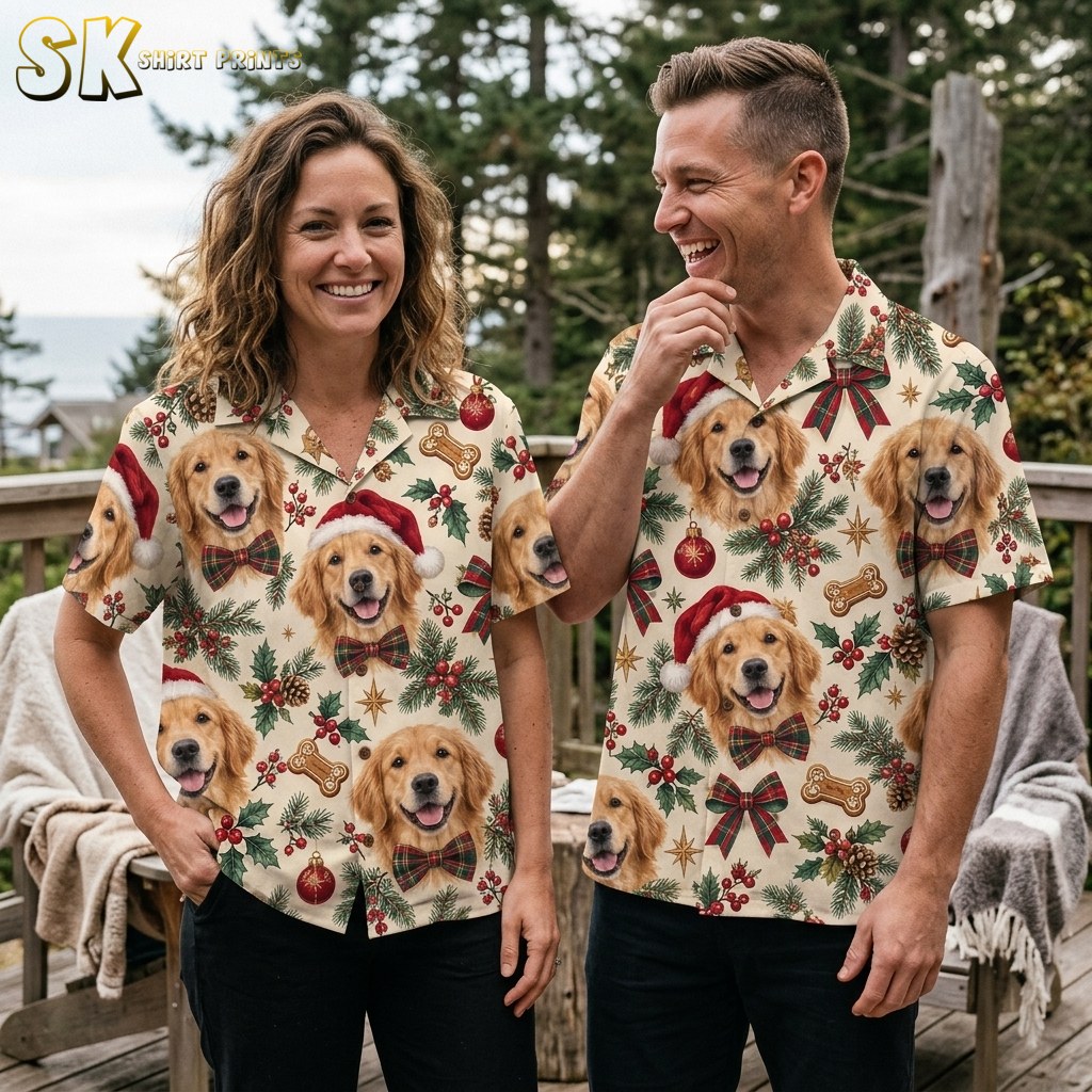 A smiling woman and man stand together on a wooden deck wearing matching Golden Retriever Christmas shirts, with pine trees and overcast sky in the background.