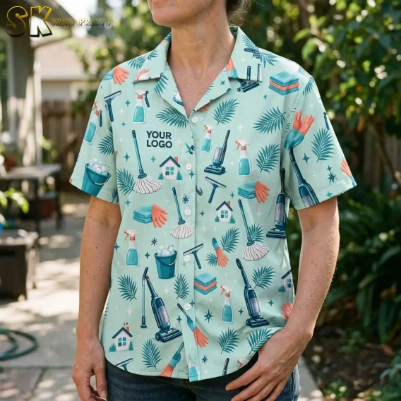 A woman photographed from the chest down wears a mint green Hawaiian shirt with your logo printed on the left chest, and the close framing reveals individual motifs including a mop, spray bottle, rubber gloves, and small house icons across the fabric.