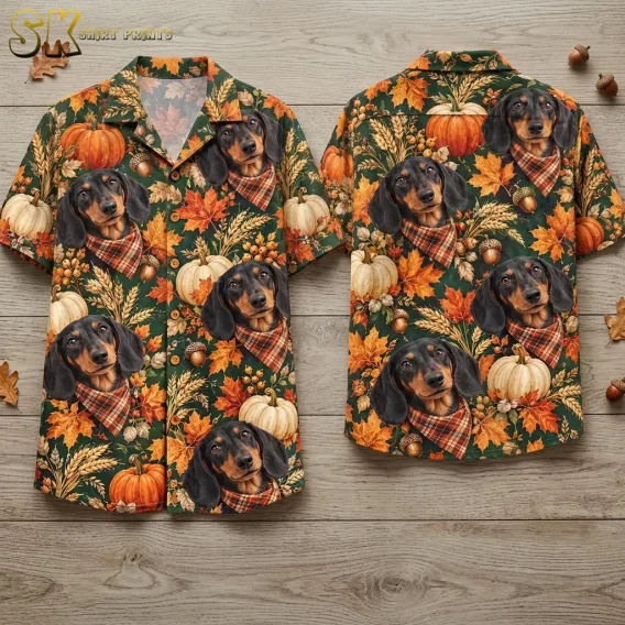 Front and back of a deep green short-sleeve shirt lie on wood boards, showing dachshunds in plaid bandanas and autumn pumpkins.