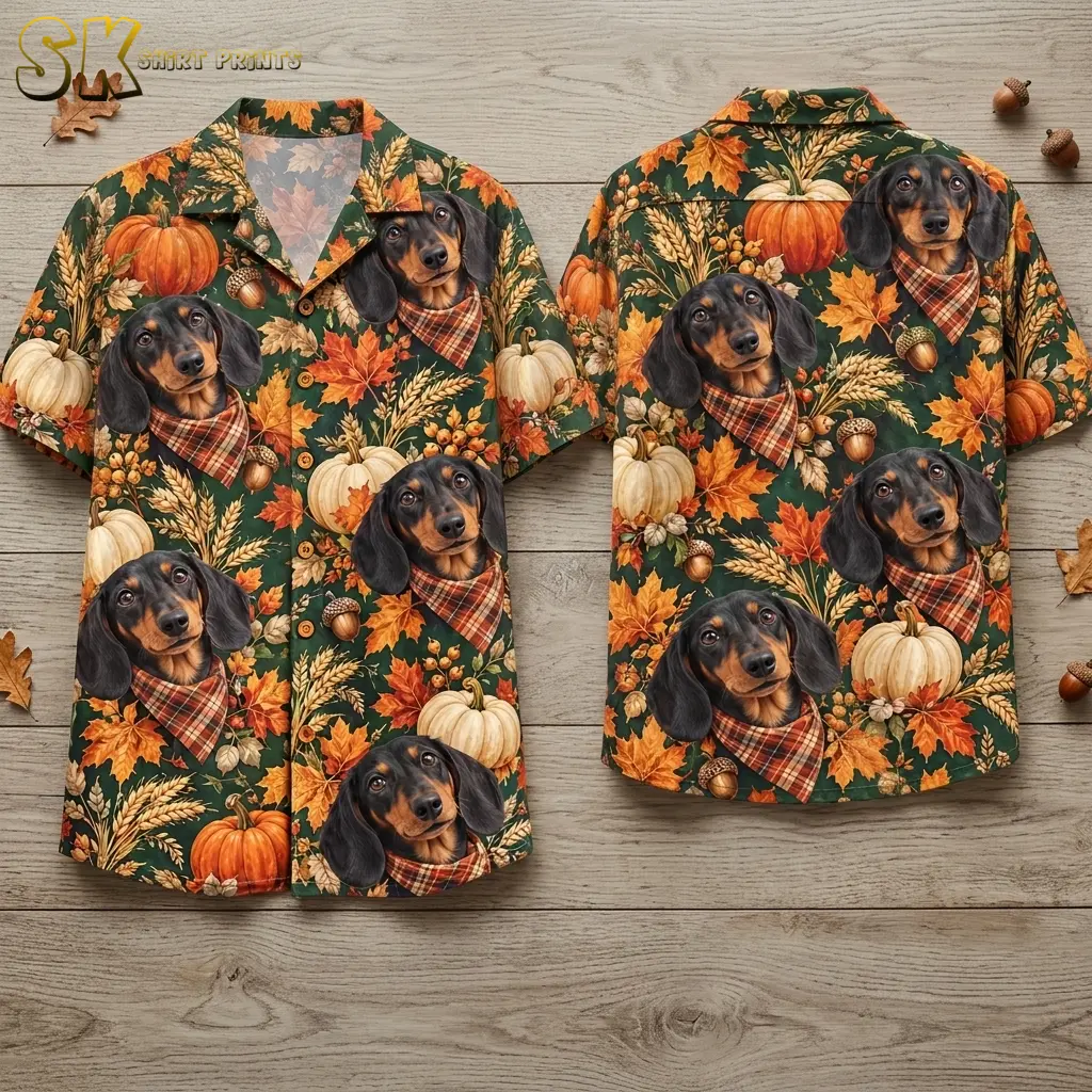 Front and back of a deep green short-sleeve shirt lie on wood boards, showing dachshunds in plaid bandanas and autumn pumpkins.