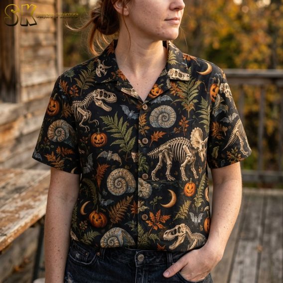 A close-up view of a woman wearing the black shirt, highlighting the detailed vintage natural history illustration style of the skeletal dinosaurs, ammonite fossils, and orange pumpkins in the print.