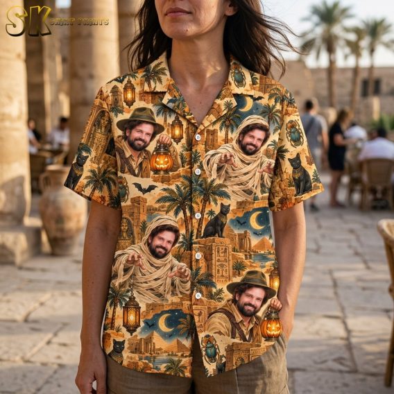 A close-up view of a woman wearing the shirt, highlighting the detailed realistic portraits of the explorer and mummy figures, hieroglyphics, and scarab beetle motifs printed on the sandy beige fabric.