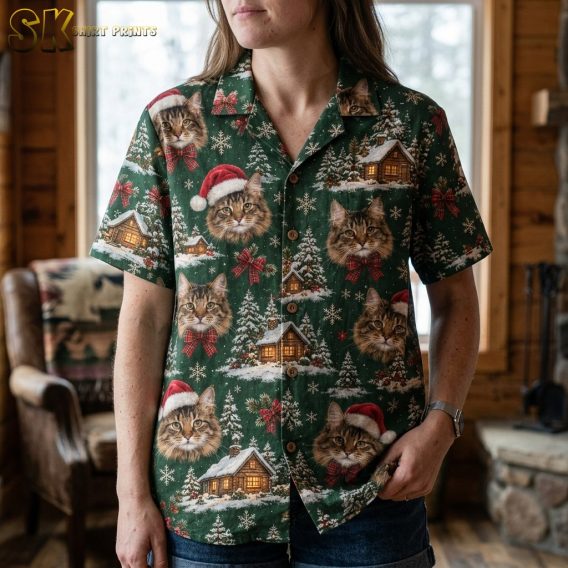A woman wearing a green cat-print holiday shirt stands near a window in a wood-paneled interior, with the close framing highlighting individual tabby cat faces, some with Santa hats and some with red plaid bow ties, spread across the front of the shirt.