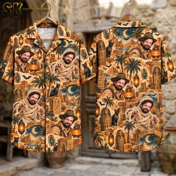 Front and back of the horror hawaiian shirt laid flat against a stone wall backdrop, with white camp-collar buttons visible on the front and the full repeat of explorer portraits, sarcophagi, palm trees, and scarab beetles spread across both sides.